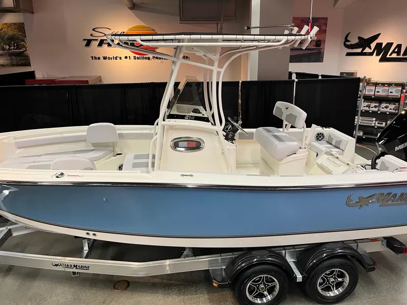 Slide: The Image of 2025 Mako 214 CC boat in showroom, blue hull, dual-axle trailer. - 2