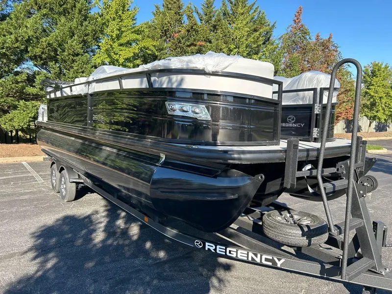 The Image of 2025 Regency 250 LE3 pontoon boat on trailer, parked outdoors, surrounded by trees. - 0