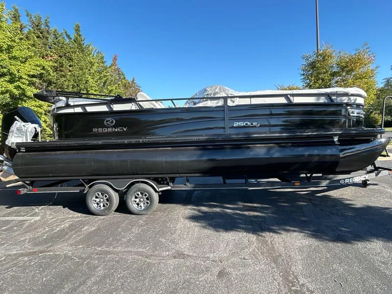 Slide: The Image of 2025 Regency 250 LE3 pontoon boat on trailer, black exterior, parked outdoors. - 1