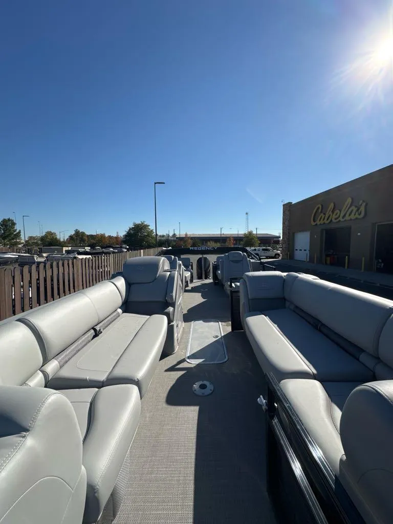 Slide: The Image of 2025 Regency 230 LE3 pontoon boat with spacious seating, parked outside Cabela's under clear blue sky. - 3