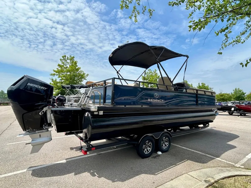 Slide: The Image of 2025 Regency 250 DL3 pontoon boat with Mercury engine, parked under a clear blue sky. - 1
