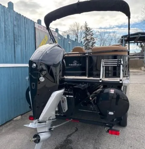 Slide: The Image of 2025 Regency 230 LE3 pontoon boat with outboard motor, parked near blue fence. - 5