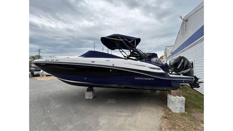 Slide: The Image of 2018 Monterey M65 boat on blocks, parked outdoors under cloudy sky. - 2