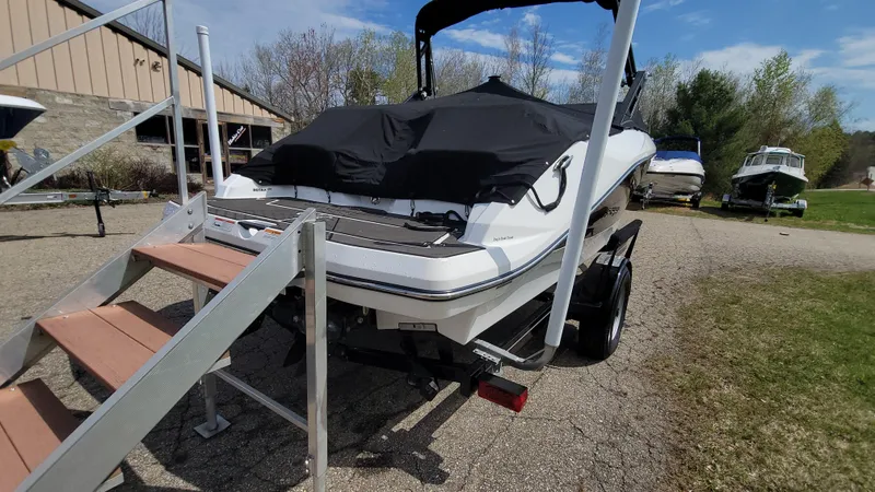 Slide: The Image of 2021 Scarab 215 ID boat on trailer with cover, parked outdoors near other boats. - 4
