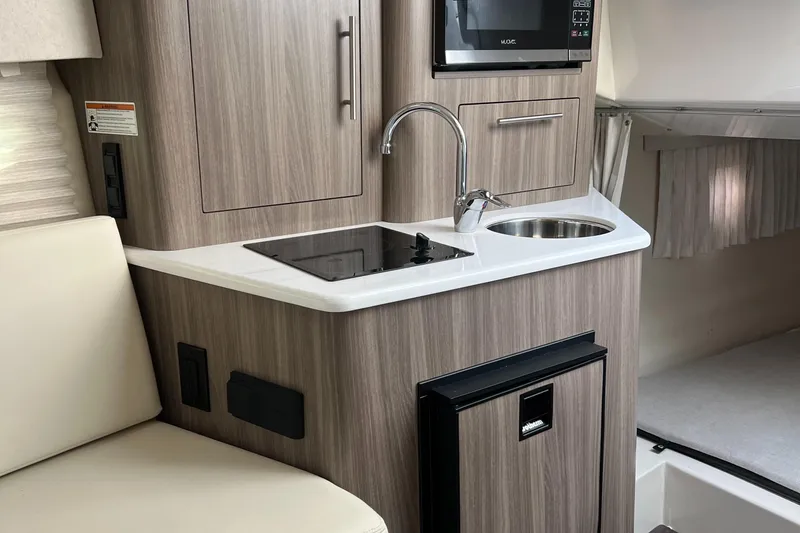 Slide: The Image of 2021 Regal 28 Express boat interior kitchen with sink, stove, and microwave. - 6