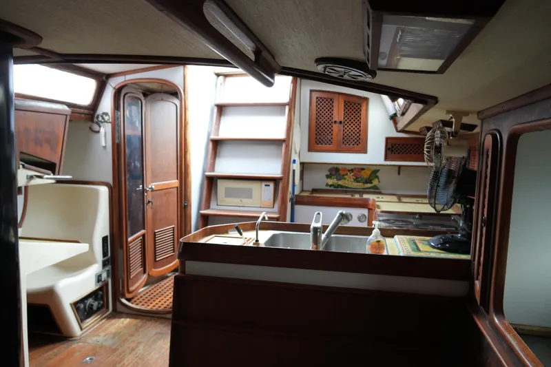 Slide: The Image of Interior of 1980 Lafitte 44 Cutter sailboat, featuring wooden cabinetry and compact kitchen area. - 29