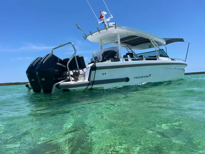 Slide: The Image of 2024 Axopar Sun Top boat on clear turquoise water, featuring dual Mercury engines. - 2