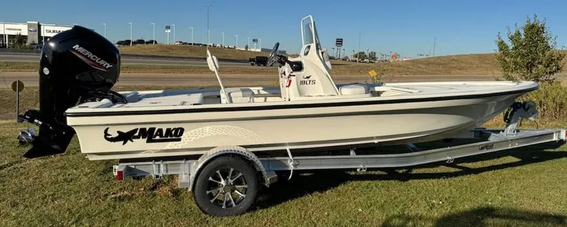 Slide: The Image of 2025 Mako 18 LTS boat on trailer, parked on grass, with Mercury outboard motor. - 2