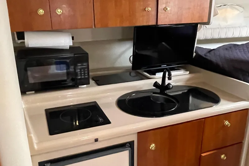 Slide: The Image of 2001 Cruisers Yachts 3075 Express kitchen with microwave, stove, sink, and wooden cabinets. - 13