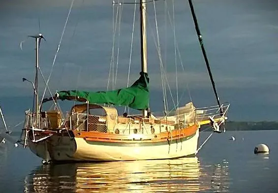 Slide: The Image of 1985 Bristol Channel Cutter sailboat with green cover on calm water. - 3