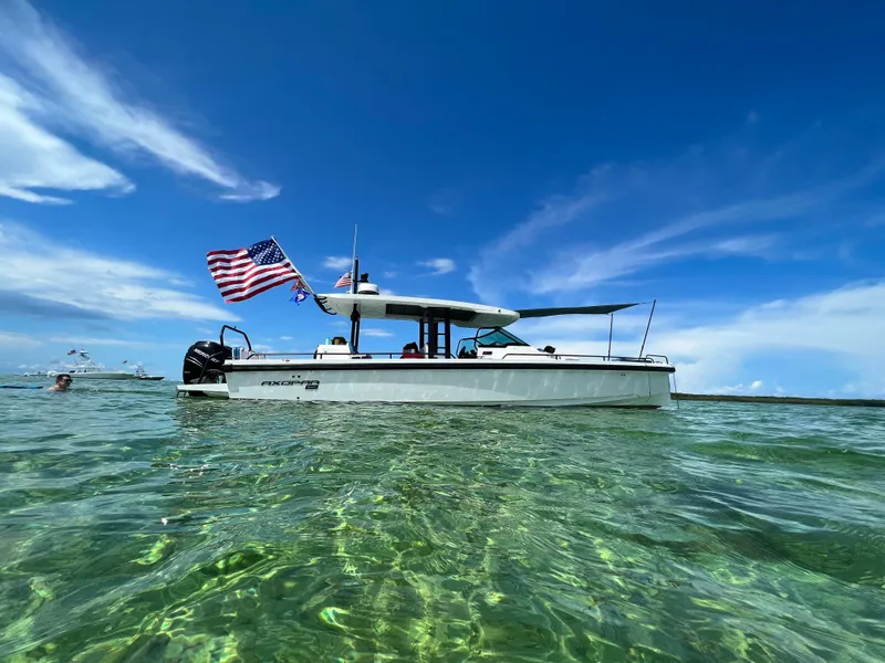 Slide: The Image of 2024 Axopar Sun Top boat on clear water, American flag waving, under blue sky. - 24