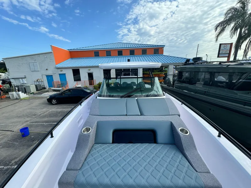 Slide: The Image of 2024 Axopar Sun Top boat with cushioned seating, parked near a building under a blue sky. - 9