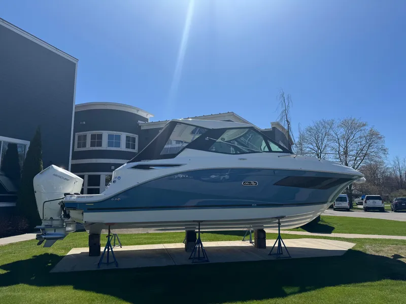 Slide: The Image of 2025 Sea Ray Sundancer 320 Coupe displayed outdoors on stands, under clear blue sky. - 3