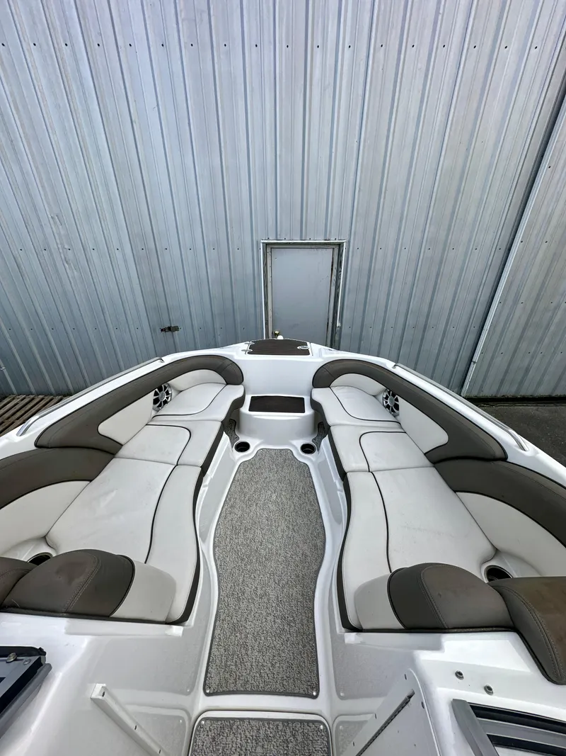 Slide: The Image of 2012 Yamaha Boats 242 Limited S interior with white and gray seating, docked by metal wall. - 12
