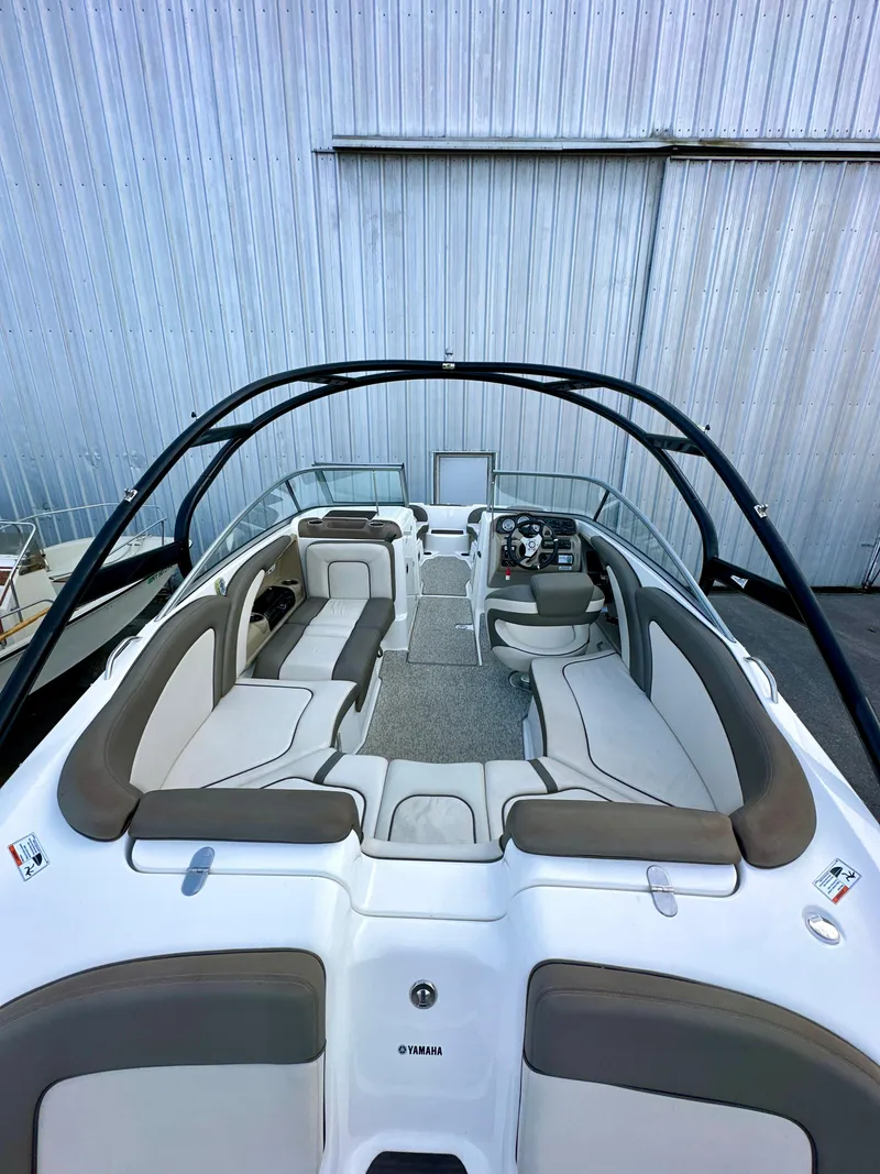 Slide: The Image of 2012 Yamaha Boats 242 Limited S interior with seating and helm, docked near a metal building. - 5