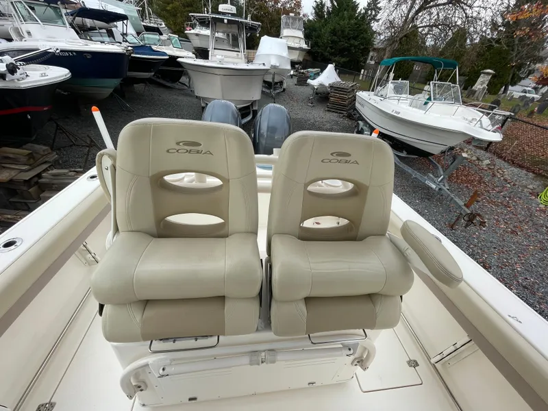 Slide: The Image of 2018 Cobia 261 boat with dual cushioned seats in a marina setting. - 12