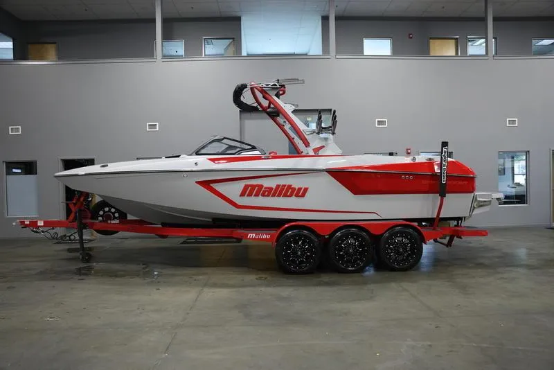 Slide: The Image of 2024 Malibu 24 MXZ boat in showroom, red and white design on trailer. - 1