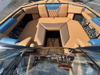 Slide: The Image of 2025 Malibu M230 boat interior with tan and blue seating, featuring a central table with cup holders. - 16