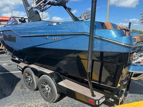 Slide: The Image of 2025 Malibu M230 boat on trailer, blue and black design, parked outdoors. - 25