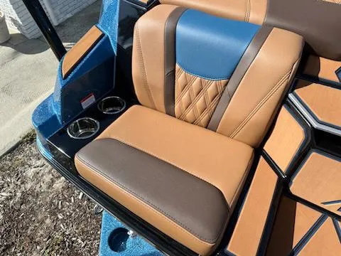 Slide: The Image of 2025 Malibu M230 boat seat with tan and blue leather upholstery, featuring cup holders. - 29