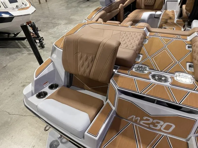 Slide: The Image of 2025 Malibu M230 boat interior with tan and white seating, stylish design, and cup holders. - 11
