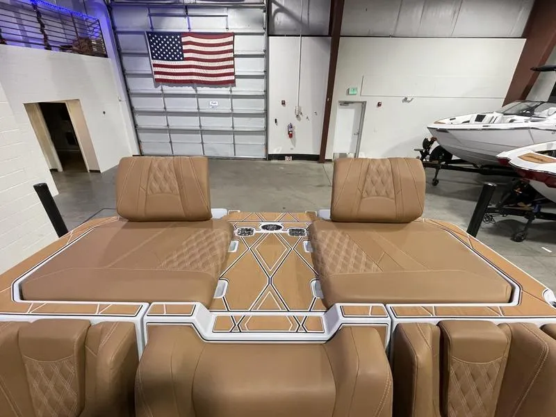 Slide: The Image of 2025 Malibu M230 boat interior with tan upholstery in a showroom. - 16