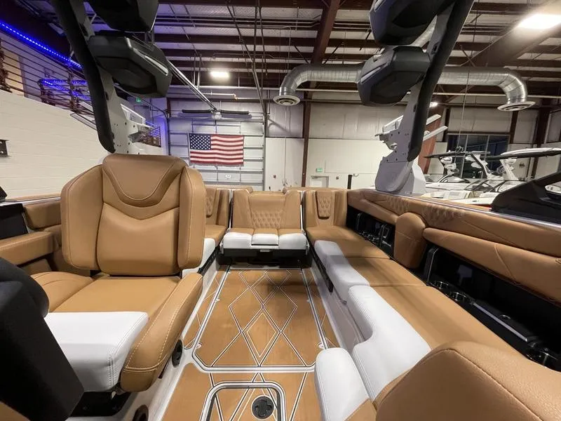 Slide: The Image of 2025 Malibu M230 boat interior with tan and white seating, in a showroom with an American flag. - 27