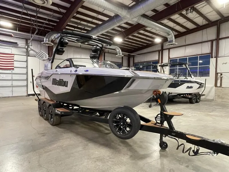 Slide: The Image of 2025 Malibu M230 boat in showroom, sleek design, on trailer. - 4