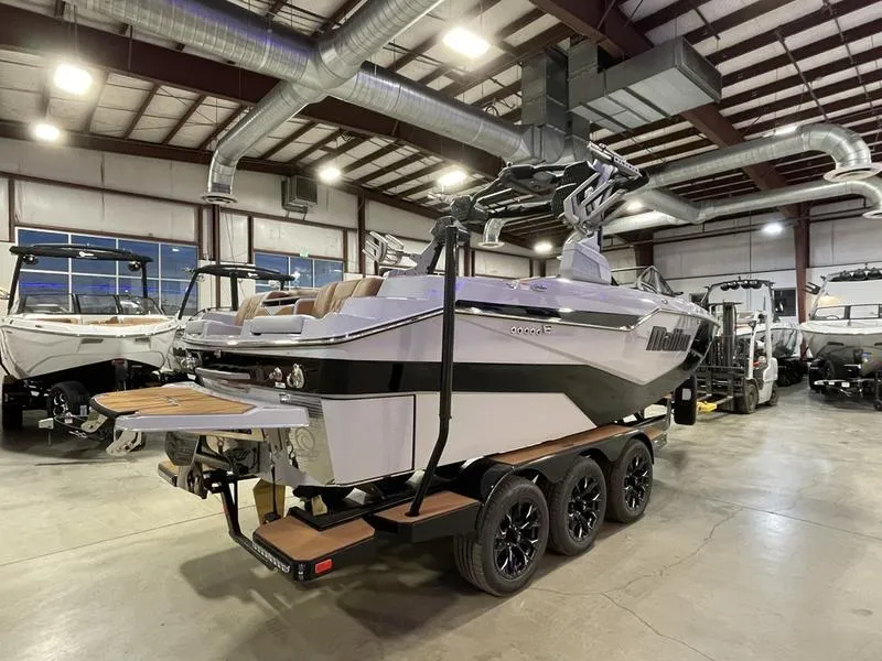 Slide: The Image of 2025 Malibu M230 boat on trailer in showroom with industrial ceiling. - 7