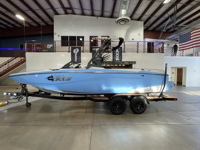 Slide: The Image of 2025 Axis A225 boat in showroom, blue exterior, on trailer, industrial setting. - 1