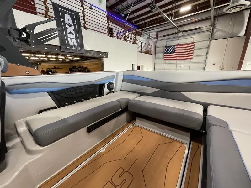 Slide: The Image of 2025 Axis A225 boat interior with gray seating, wooden flooring, and American flag in the background. - 14