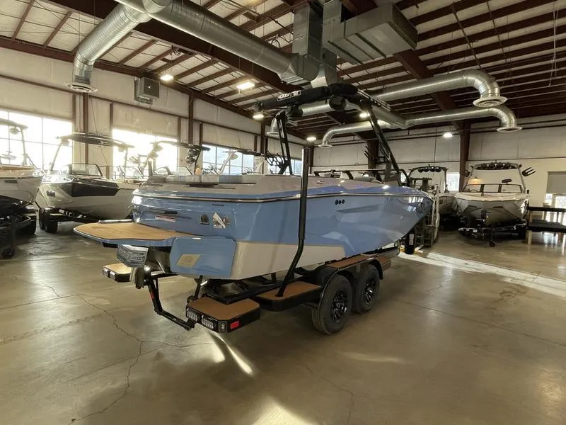Slide: The Image of 2025 Axis A225 boat in showroom, blue exterior, on trailer, surrounded by other boats. - 7