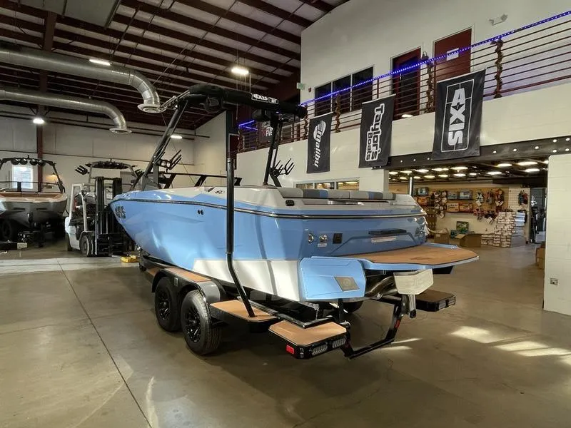 Slide: The Image of 2025 Axis A225 boat in showroom, blue exterior, on trailer, surrounded by banners and equipment. - 9