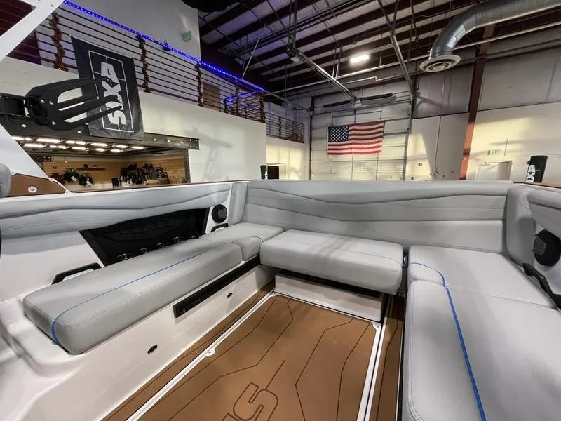 Slide: The Image of 2025 Axis A225 boat interior with gray seating, wooden floor, and American flag in showroom. - 15