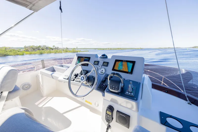 Slide: The Image of 2021 Beneteau Swift Trawler 41 helm with navigation screens, steering wheel, and serene water view. - 41