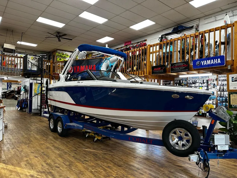 Slide: The Image of 2025 Cobalt CS23 Surf boat displayed indoors on a trailer. - 0