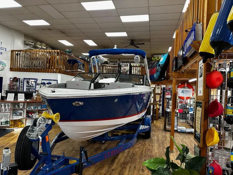 Slide: The Image of 2025 Cobalt CS23 Surf boat displayed in a showroom with boating accessories. - 1