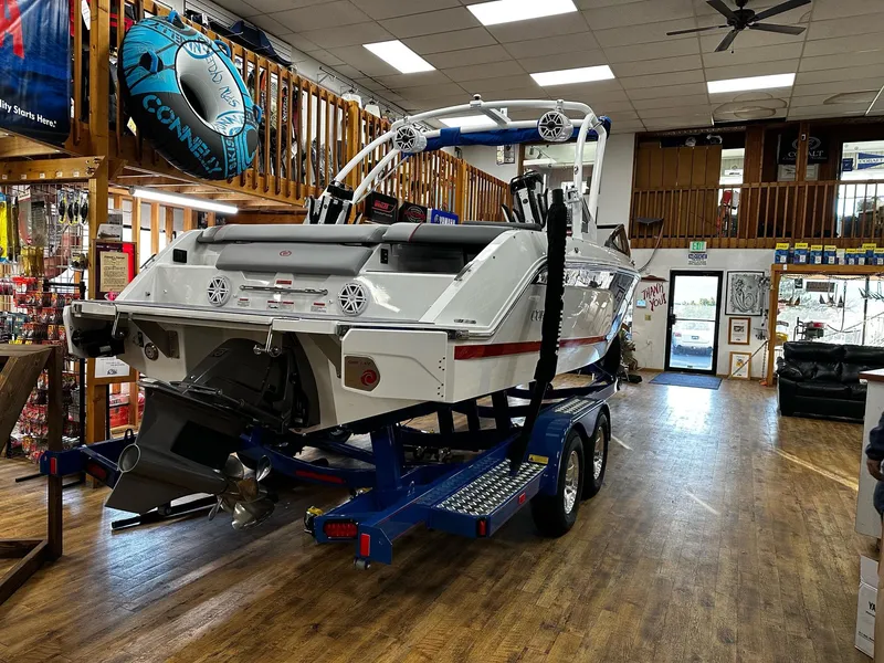 Slide: The Image of 2025 Cobalt CS23 Surf boat displayed indoors on a blue trailer. - 2
