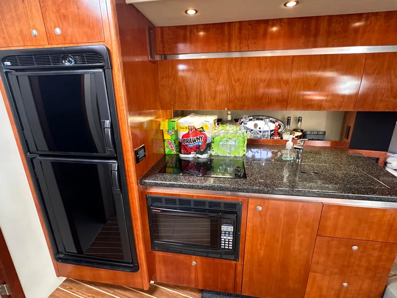 Slide: The Image of 2006 Cruisers Yachts 420 Express kitchen with wood cabinetry, granite countertop, fridge, and microwave. - 34