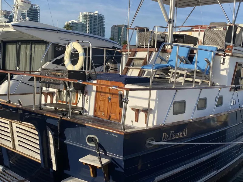 Slide: The Image of 1983 DeFever 41 yacht docked, featuring a spacious deck with blue chairs and a life ring. - 3