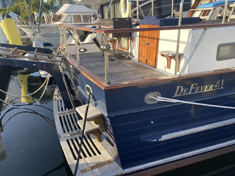 Slide: The Image of 1983 DeFever 41 yacht docked at marina, featuring wooden deck and blue hull. - 6