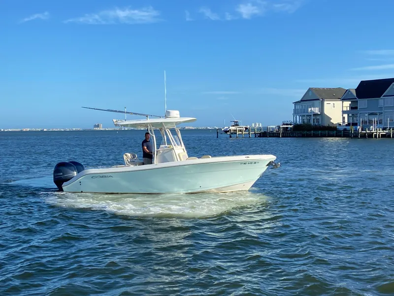 Slide: The Image of 2018 Cobia 237 CC boat cruising near waterfront homes on a sunny day. - 2