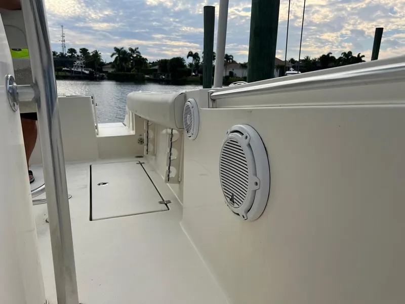 Slide: The Image of 2015 Cobia 237 Center Console boat deck with speakers, docked by a scenic waterfront. - 12