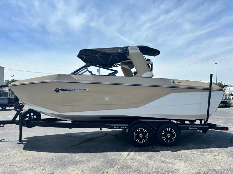 Slide: The Image of 2025 Nautique Super Air Nautique G23 boat on trailer, beige and white, under clear sky. - 0