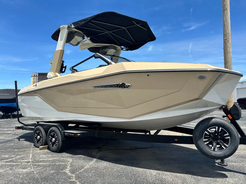 Slide: The Image of 2025 Nautique Super Air Nautique G23 boat on trailer, beige color, under clear blue sky. - 10