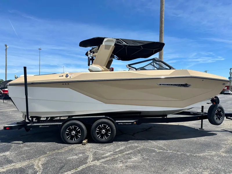 Slide: The Image of 2025 Nautique Super Air Nautique G23 boat on trailer, beige and white, parked outdoors. - 3