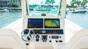 Slide: The Image of 2025 Grady-White Canyon 306 boat dashboard with dual screens and steering wheel, docked by the water. - 5