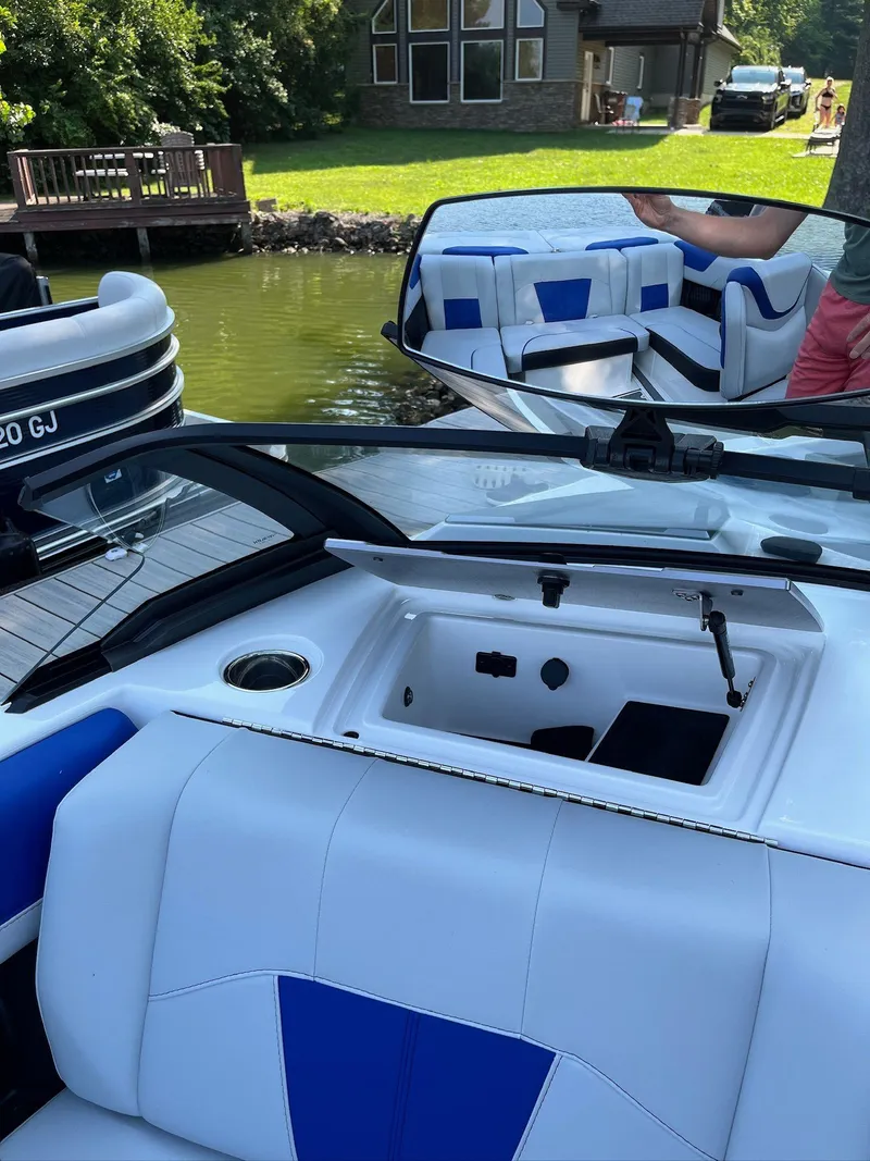 Slide: The Image of 2024 Malibu 20VTX boat interior with blue and white seating, docked near a house. - 10