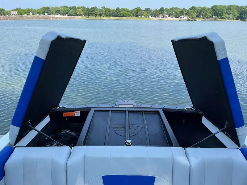 Slide: The Image of 2024 Malibu 20VTX boat with open storage compartments on a serene lake. - 11