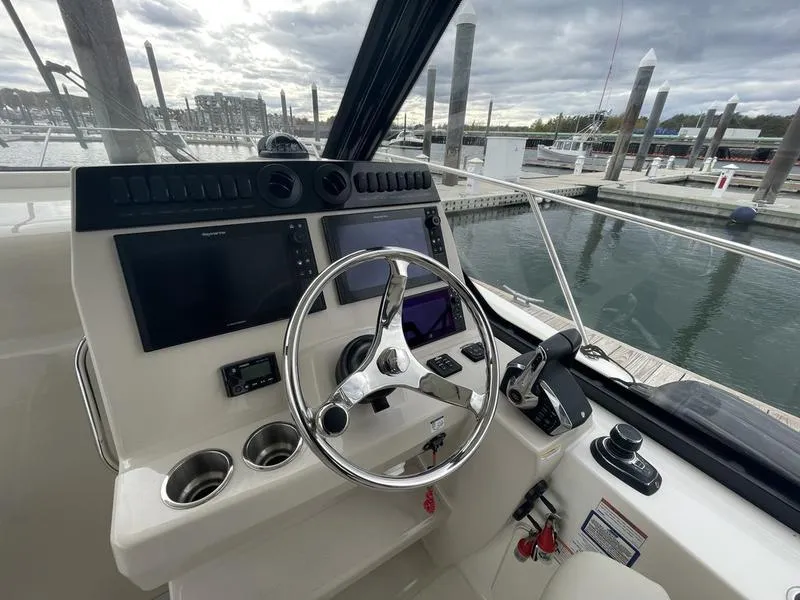 Slide: The Image of 2023 Boston Whaler 325 Conquest helm with modern controls and marina view. - 11